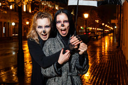 Outdoor night portrait of two young beautiful  girl holding transparent umbrella with garland, posing in street of european city. rain.の写真素材