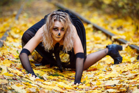 Halloween horror composition. Scaring dark haired girl in black dress with sword in the smoke and  in the forest. Gothic darkness, ghost in the yellow autumn forestの写真素材
