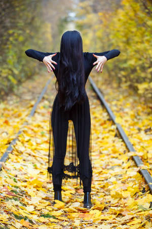 Halloween horror composition. Scaring dark haired girl in black dress with sword in the smoke and ...