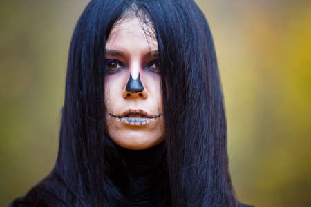 Halloween horror composition. Scaring dark haired girl in black dress with sword in the smoke and  in the forest. Gothic darkness, ghost in the yellow autumn forestの写真素材