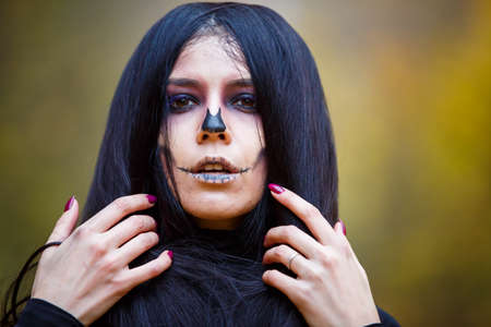 Halloween horror composition. Scaring dark haired girl in black dress with sword in the smoke and  in the forest. Gothic darkness, ghost in the yellow autumn forestの写真素材