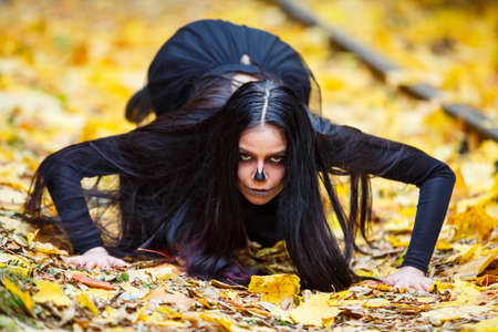 beautiful young girl in a long black dress jumping from the seat. Day, park with yellow autumn foliageの写真素材