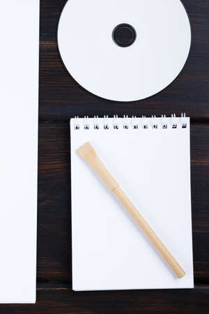 Blank notebook, CD disk, pen, list of paper on dark background mockup designの写真素材