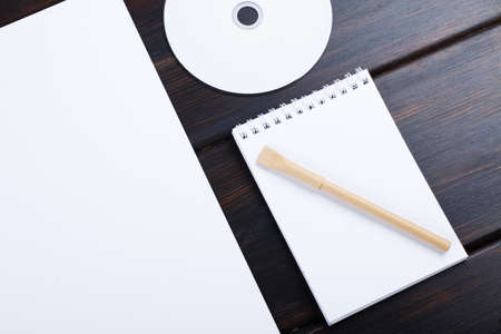 Blank notebook, CD disk, pen, list of paper on dark background mockup design