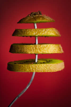 Sliced kiwi on a fork with red background.