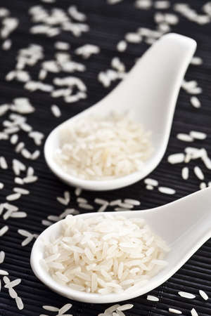 Raw rice on a two white spoons with a black bamboo background.の写真素材