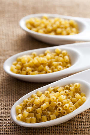 Italian pasta tubes on a white ceramic spoons.の写真素材