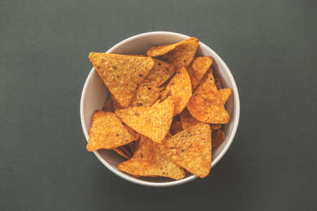 White bowl of nachos in a green background.
