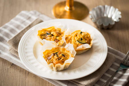 Delicious mini quiche with vegetables and pumpkin on a wooden table.
