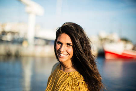Portrait of attractive young woman smiling at camera while standing on pier