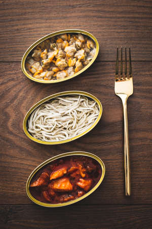 Traditional spanish canned food, pickled squid, surimi elvers and cockles on a wooden table.
