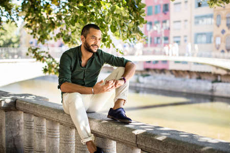 Side view of smiling bearded man sitting on fence under trees.Summer timeの写真素材