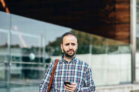 Bearded man with leather bag looking away while standing outdoor. Modern building on backgroundの写真素材