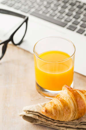 Orange juice, croissant on napkin, glasses near laptop office.の写真素材