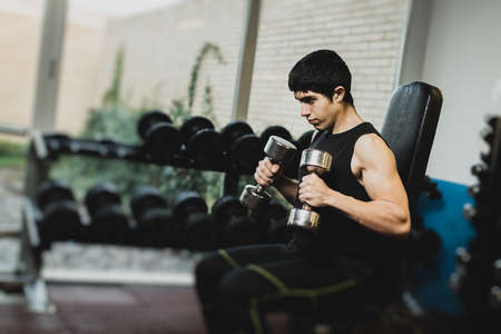 Muscular man doing exercise with dumbbells in gymの写真素材