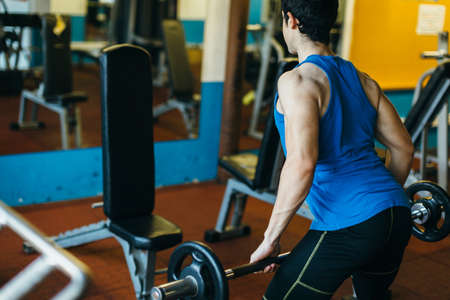 Young sportsman training with weights in gym. Unrecognizable