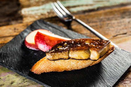 Snack of fried foie gras and red apple on a slice of bread.の写真素材