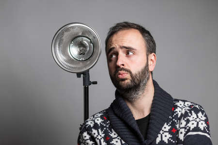 Portrait of adult bearded man holding camera on outstretched hand taking selfie and shows thumb up against studio flashlightの写真素材