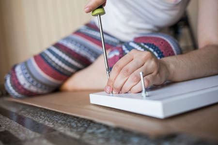 Close up of unrecognizable person in colorful leggings tightens screw with a screwdriver lying on the floorの写真素材