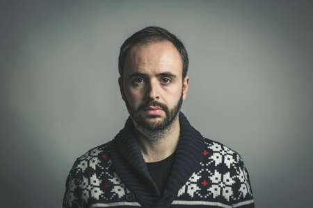 Portrait of adult bearded man wearing blue wool sweater with emotion of sorrow on face looking awayの写真素材
