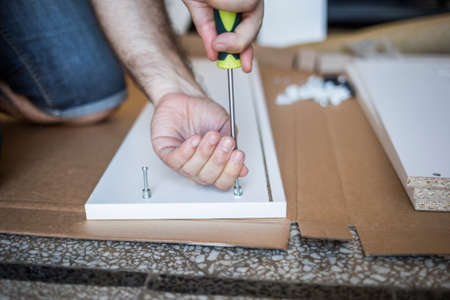 Close up of unrecognizable person in blue jeans tightens screw with a screwdriver sitting on the floorの写真素材