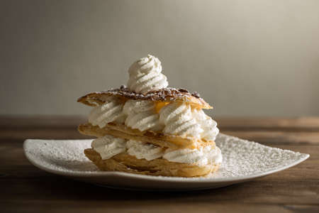 Close up of creamy desert with whipped cream decorative powder on plate on wooden table.の写真素材