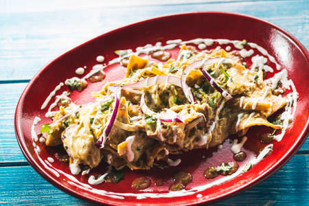 Delicious Mexican Chilaquiles placed on a red plate. Blue wooden table.