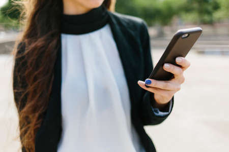 Hands of woman wearing formal clothes browsing phone outside.の写真素材