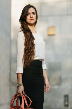Young confident woman in elegant outfit holding leather bag and looking away.の写真素材