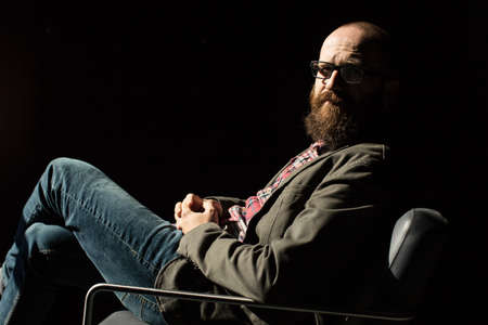 Side view of trendy man sitting confidently in chair in sun ray.の写真素材