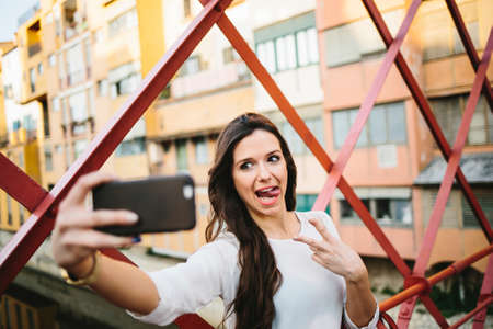 Young girl making faces while taking selfie on bridge.