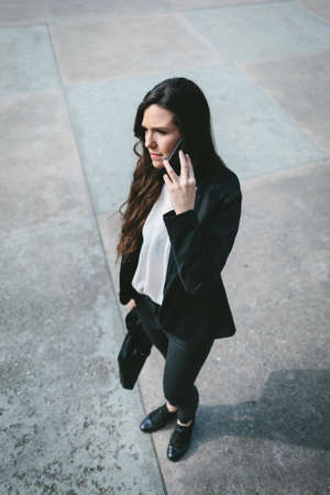 Cheerful formal dressed woman talking on phone. Vertical outdoors shot.の写真素材