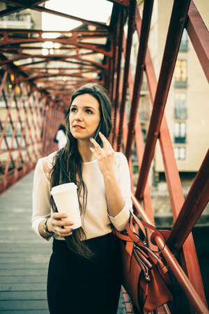 Young trendy girl talking phone and looking away while standing on bridge.の写真素材