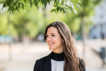 Cheerful businesswoman standing under the tree and smiling. Horizontal outdoors shot.の写真素材