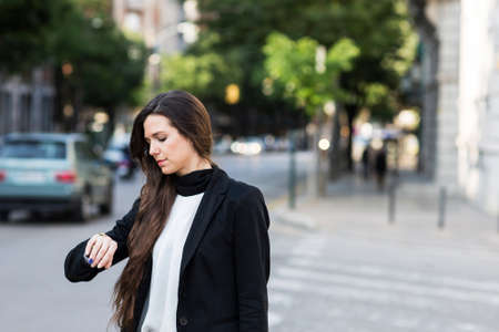 Adult businesswoman looking at the wrist watch standing on a crossroad.の写真素材