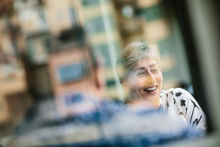 Shot through glass of cheerful laughing mature woman sitting in restaurant with man.の写真素材