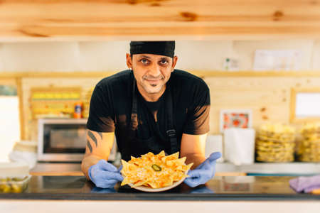 Smiling man in uniform smiling at camera and showing order standing in food truck.の写真素材