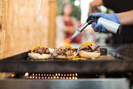 Chef in gloves using gas torch and burning cheese while making burgers.の写真素材