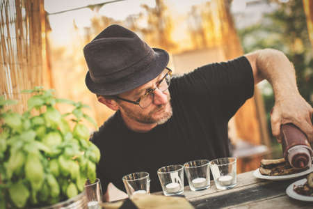 Man in glasses and hat roasting meat on grill outside.の写真素材