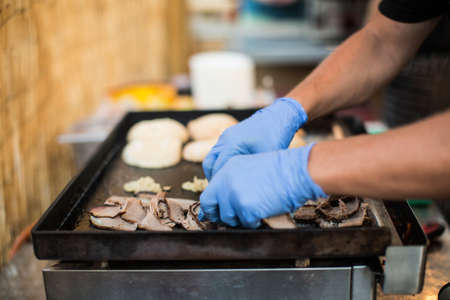 Crop faceless shot of person in gloves pouring cheese on burgers.の写真素材