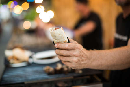 Crop male hand of vendor holding made burrito on blurred background of food truck.の写真素材