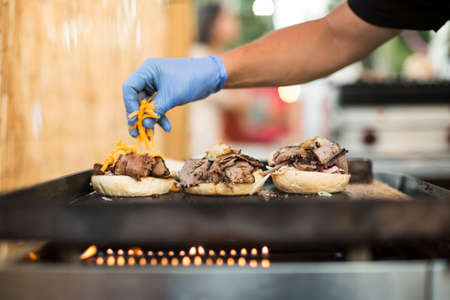 Crop faceless shot of person in gloves pouring cheese on burgers.の写真素材