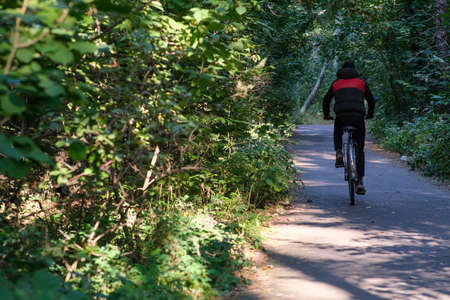 Cycling through the park. A man in a jacket rides a bicycle along the path. Cycling in the woods.