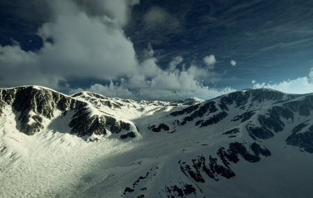 Behold the Majestic Aerial View of the SnowCapped Mountains Beneath a Clear Blue Skyの写真素材