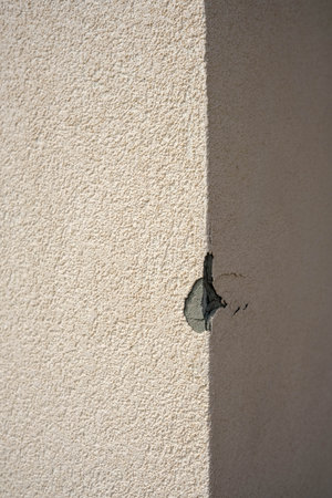 A close-up shot reveals a damaged building exterior with a visible crack and missing plaster on a light-colored textured wall.の写真素材