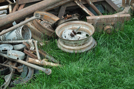Pile of rusted metal scrap and old machinery parts on green grass, depicting industrial decay.の写真素材