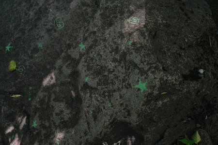 Dark, textured rock surface adorned with scattered green chalk symbols and natural sunlight dappling.の写真素材