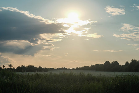 Sunrays Over Rural Landscape at Sunset. Golden light breaks through clouds illuminating a field and distant tree line.の写真素材