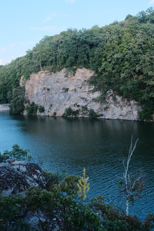 Majestic granite quarry with steep rock faces rising above tranquil blue-green water, surrounded by lush, dense forest.の写真素材