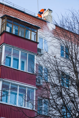 Parkovaya Street, Balashikha, Russia-February 19, 2021. Snow removal. A worker removes snow with a shovel from the roof of a building after a snowfall.のeditorial素材